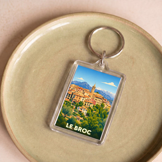 Porte-clés souvenir de la ville de Le Broc avec une illustration stylisée du village et des montagnes.