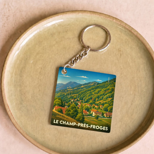 Porte-clés souvenir de la ville de Le Champ-près-Froges avec une illustration stylisée de son paysage montagneux.