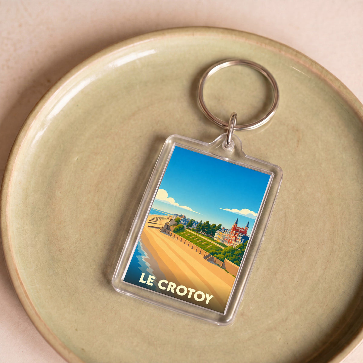 Porte-clés souvenir de la ville du Crotoy avec une illustration stylisée d'une plage et de bâtiments colorés.