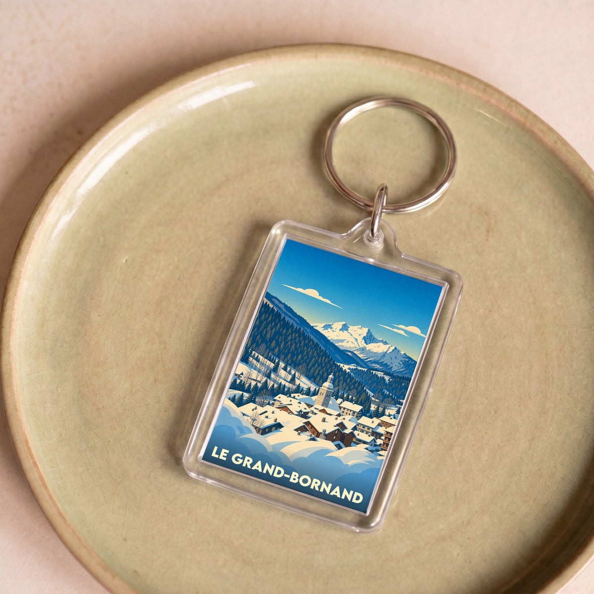 Porte-clés souvenir de la ville du Grand-Bornand avec une illustration stylisée d'un village de montagne enneigé.