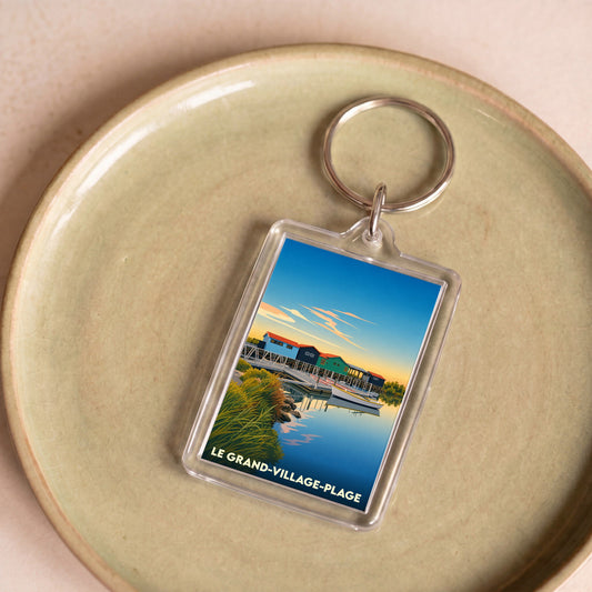 Porte-clés souvenir de la ville de Le Grand-Village-Plage avec une illustration stylisée de cabanes colorées sur l'eau.