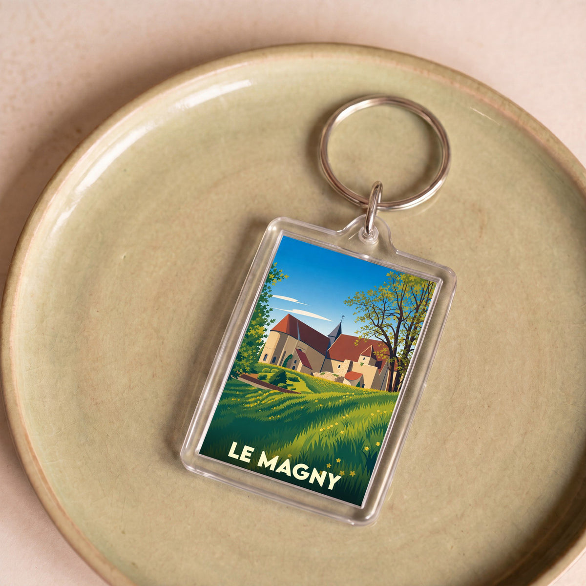 Porte-clés souvenir de la ville de Le Magny avec une illustration stylisée d'un paysage champêtre.