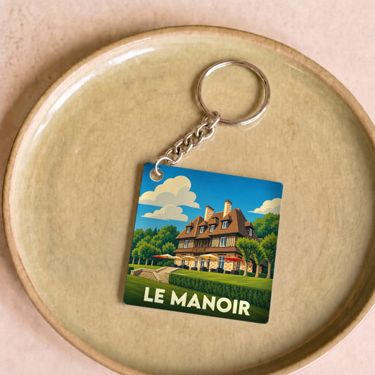 Porte-clés souvenir de la ville de Le Manoir avec une illustration stylisée.