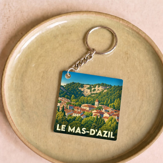 Porte-clés souvenir de la ville de Le Mas-d'Azil avec une illustration stylisée du village niché dans la verdure.