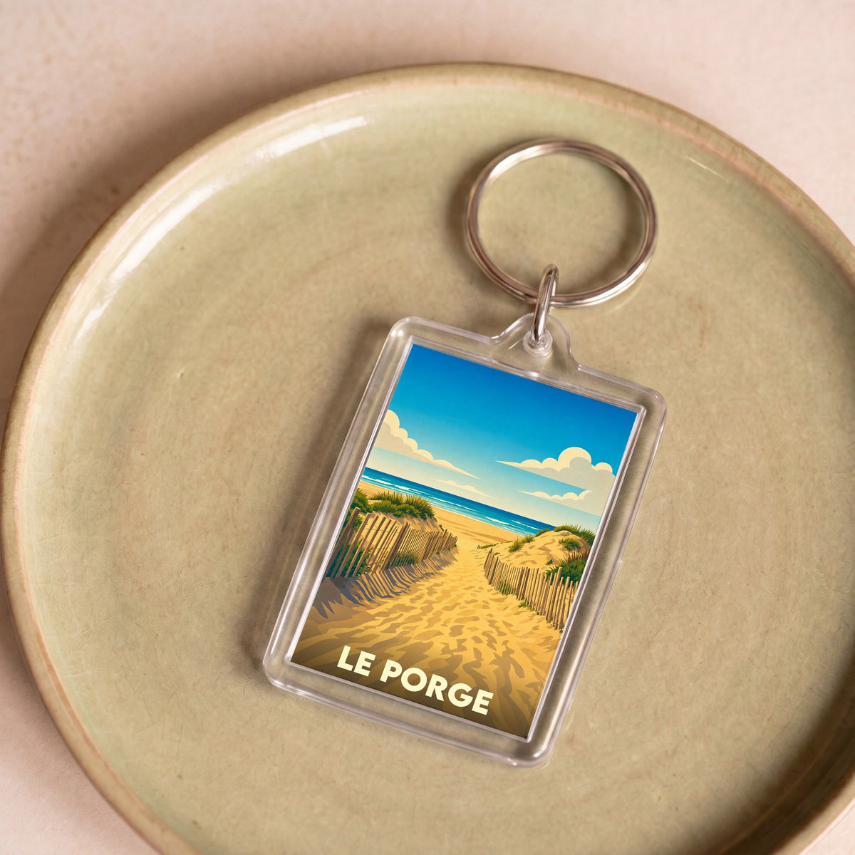 Porte-clés souvenir de la ville du Porge avec une illustration stylisée d'un chemin dunaire menant à l'océan.