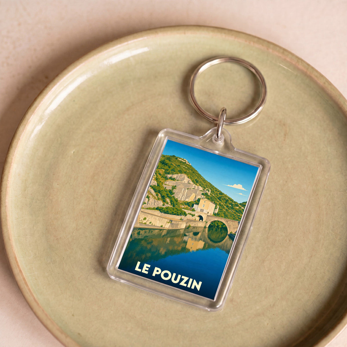 Porte-clés souvenir de la ville de Le Pouzin avec une illustration stylisée d'un pont se reflétant dans l'eau.