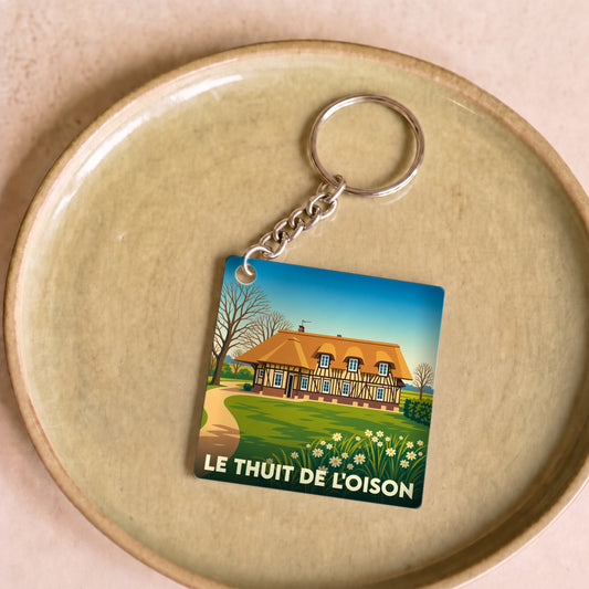 Porte-clés souvenir de la ville de Le Thuit de l'Oison avec une illustration stylisée d'une maison normande.