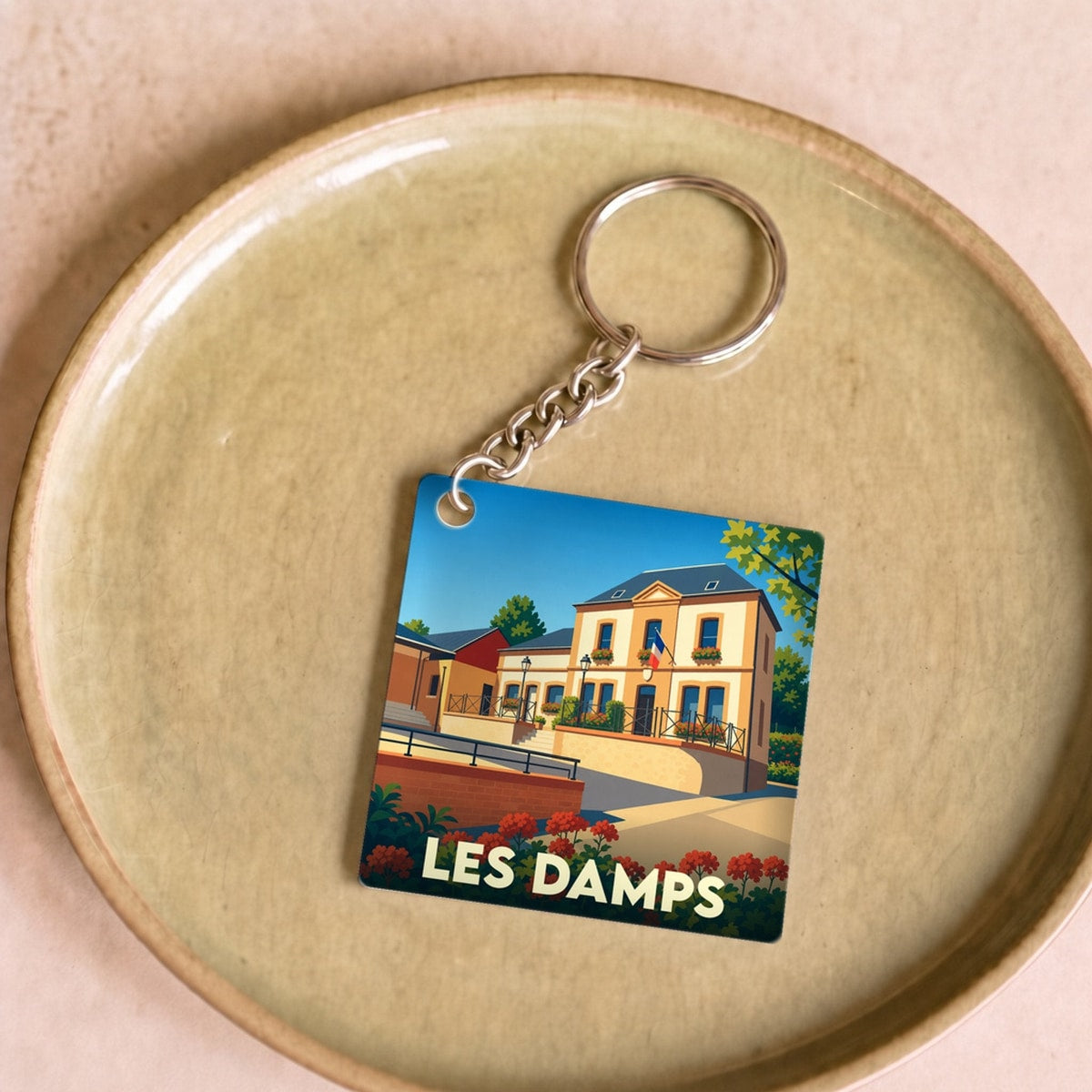 Porte-clés souvenir de la ville de Les Damps avec une illustration stylisée d'un bâtiment municipal.
