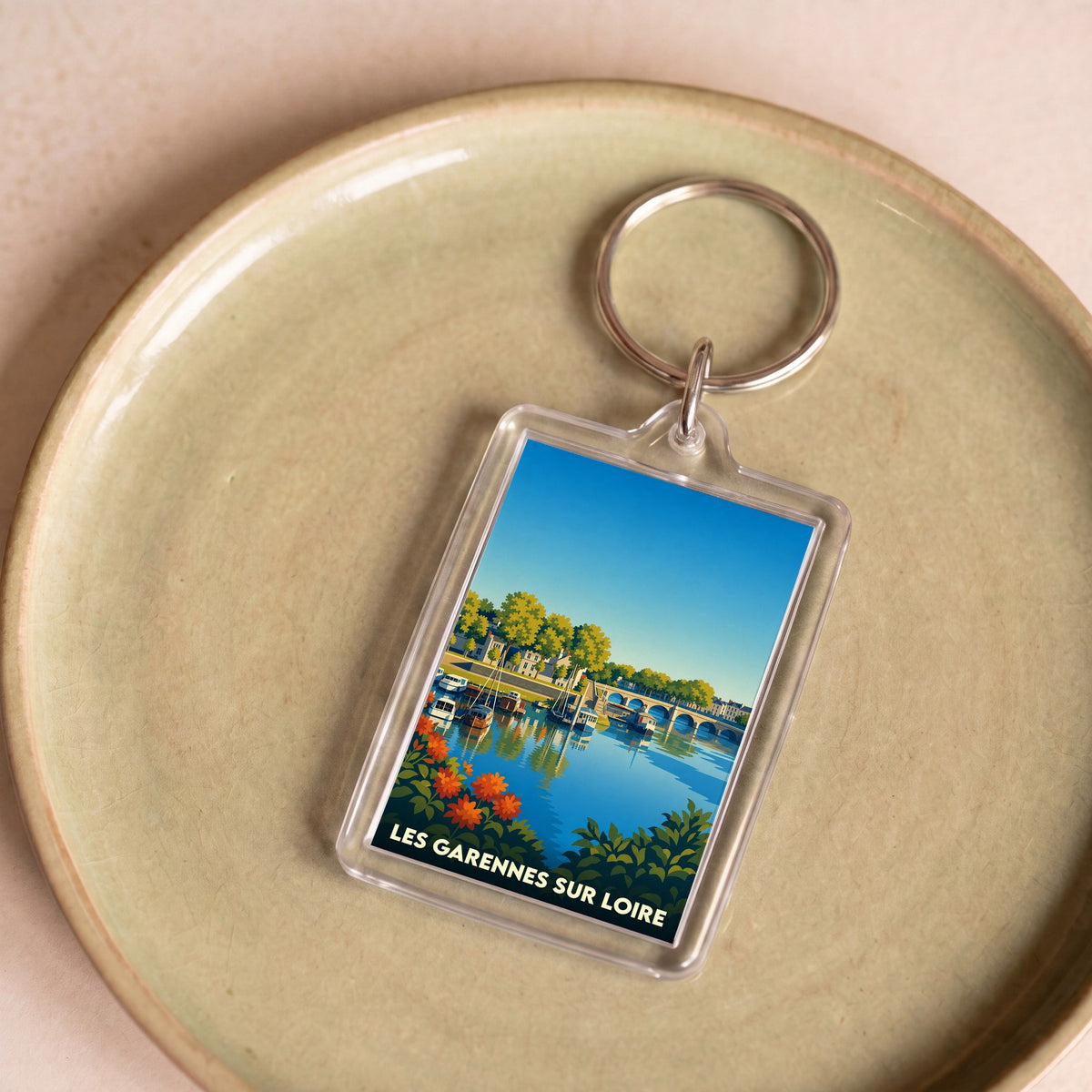 Porte-clés souvenir de la ville de Les Garennes sur Loire avec une illustration stylisée d'un paysage de bord d'eau.