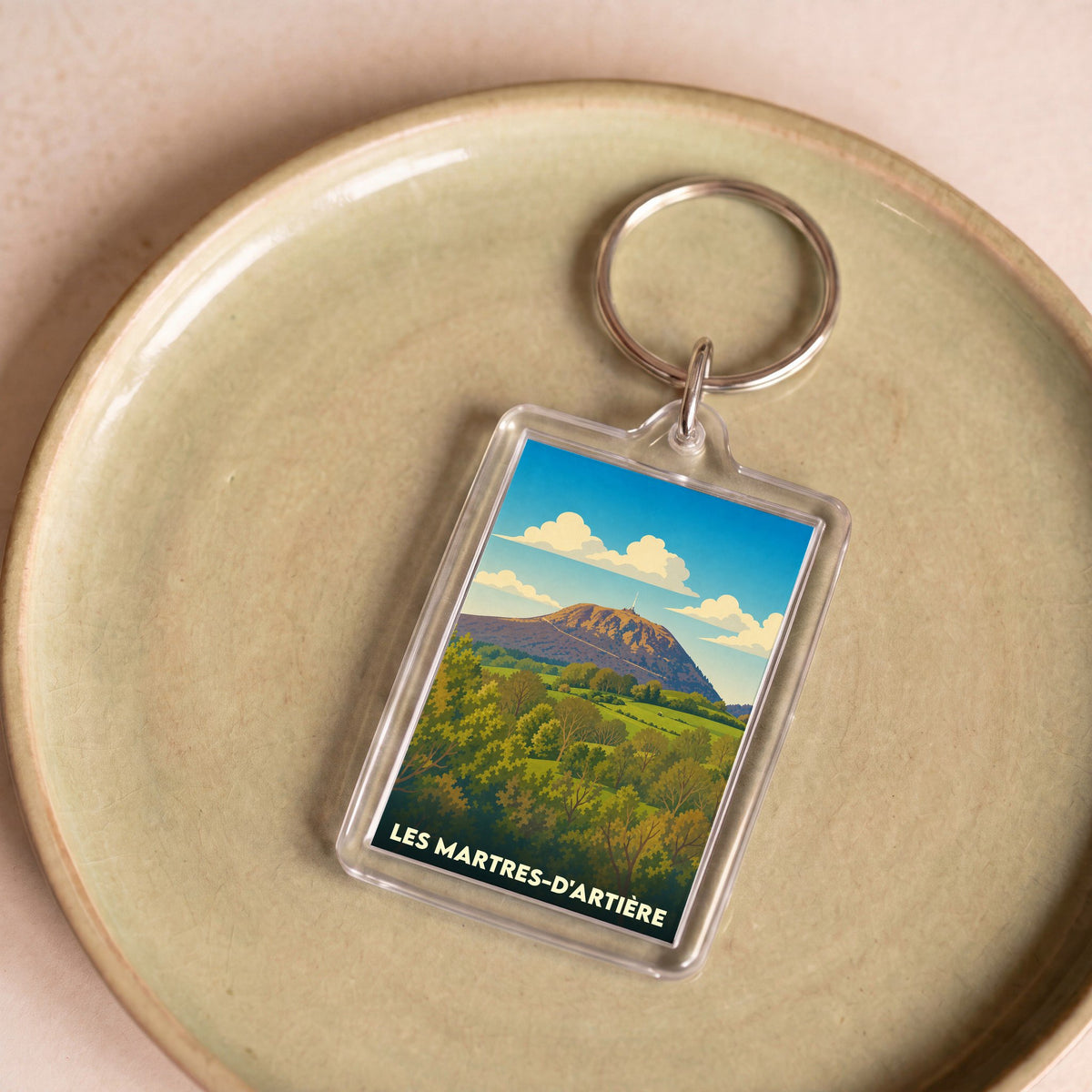 Porte-clés souvenir de la ville de Les Martres-d'Artière avec une illustration stylisée d'un paysage de montagne.