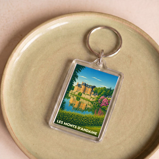 Porte-clés souvenir de la ville de Les Monts d'Andaine avec une illustration stylisée d'un château se reflétant dans l'eau.