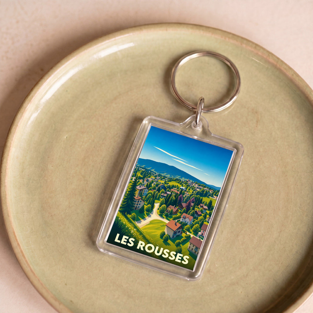 Porte-clés souvenir de la ville de Les Rousses avec une illustration stylisée d'un paysage de montagne.