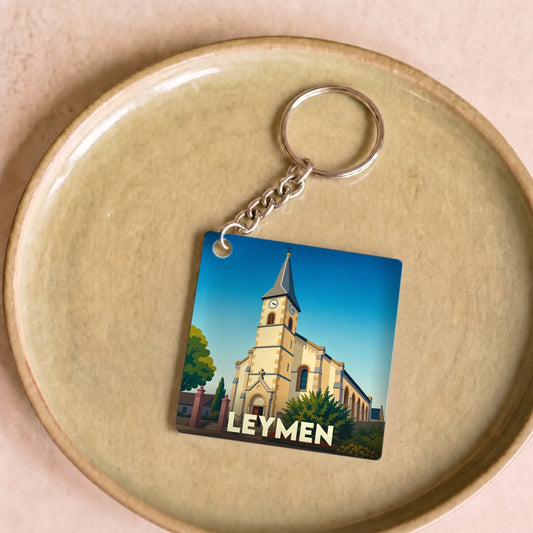 Porte-clés souvenir de la ville de Leymen illustrant une église stylisée sous un ciel bleu.