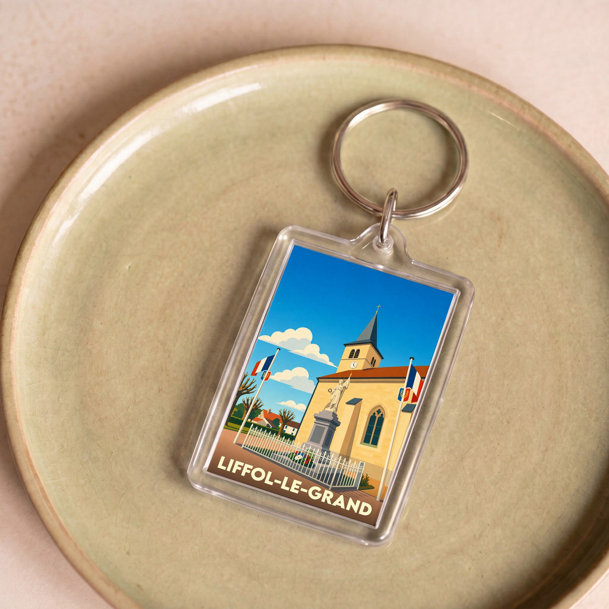 Porte-clés souvenir de la ville de Liffol-le-Grand avec une illustration stylisée de son église et de son monument.
