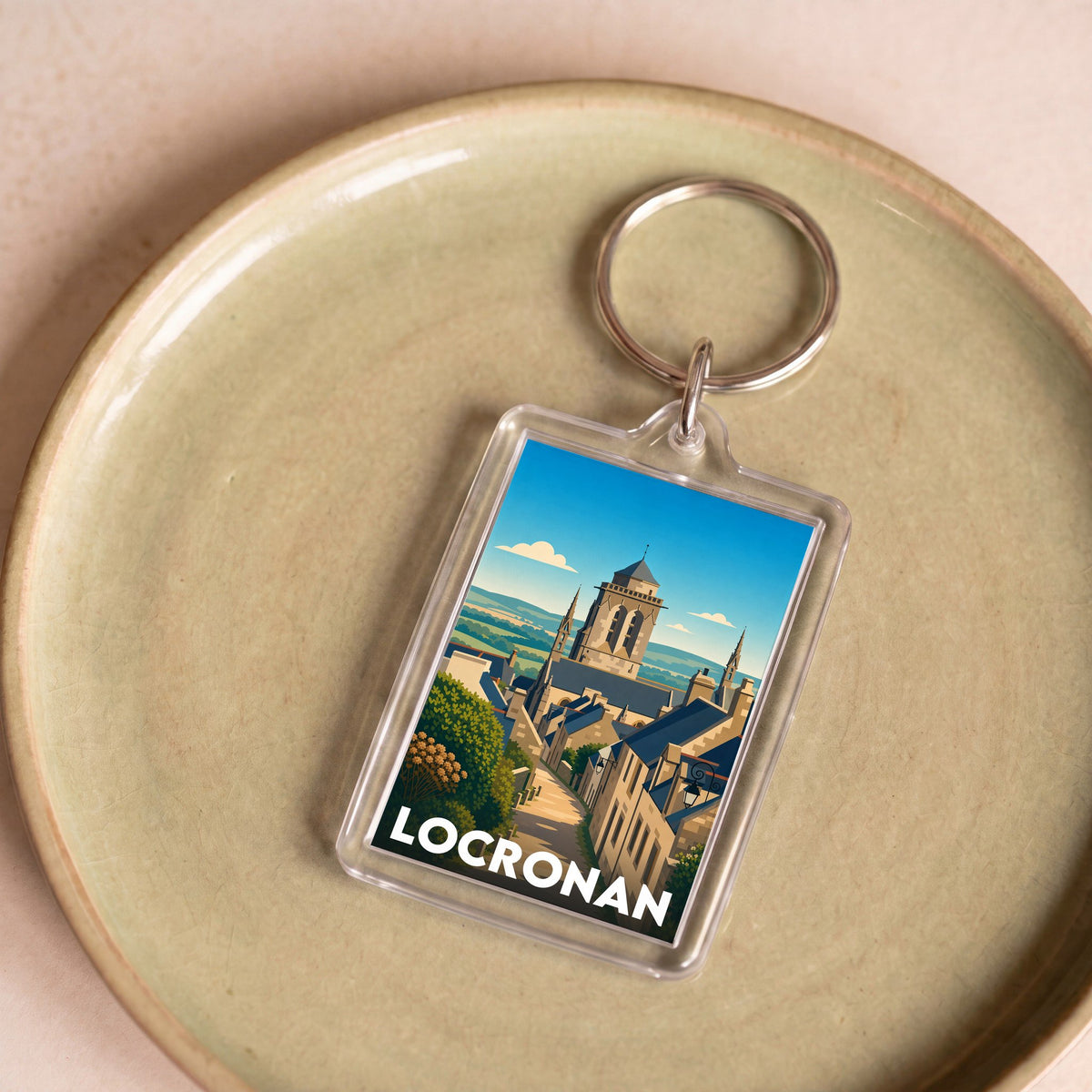 Porte-clés souvenir de la ville de Locronan avec une illustration stylisée de son église et de ses maisons en pierre.