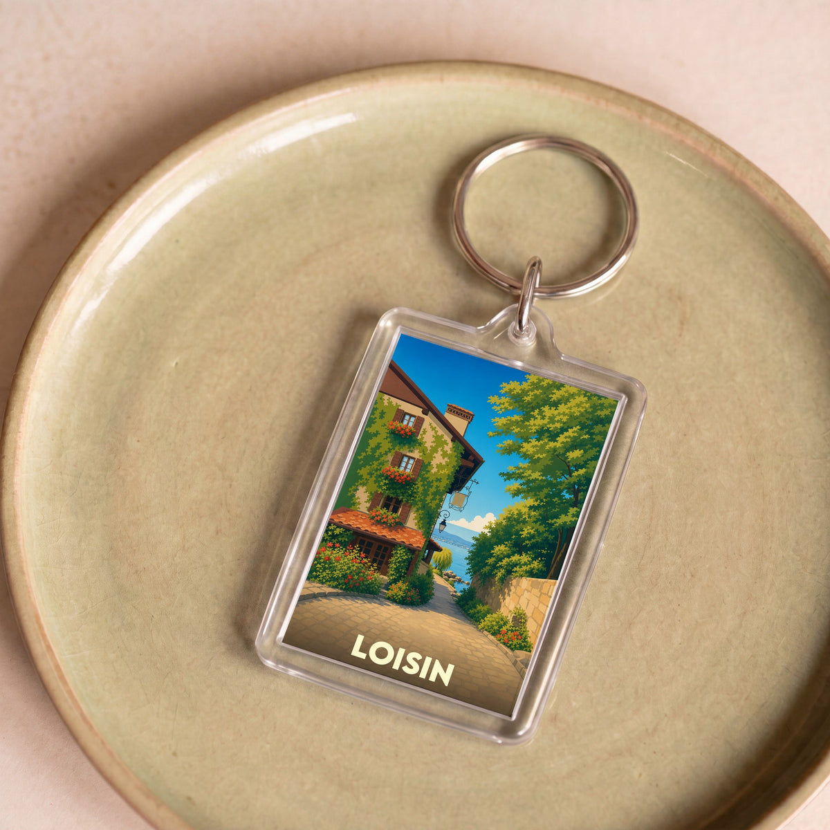 Porte-clés souvenir de la ville de Loisin avec une illustration stylisée d'une rue fleurie.