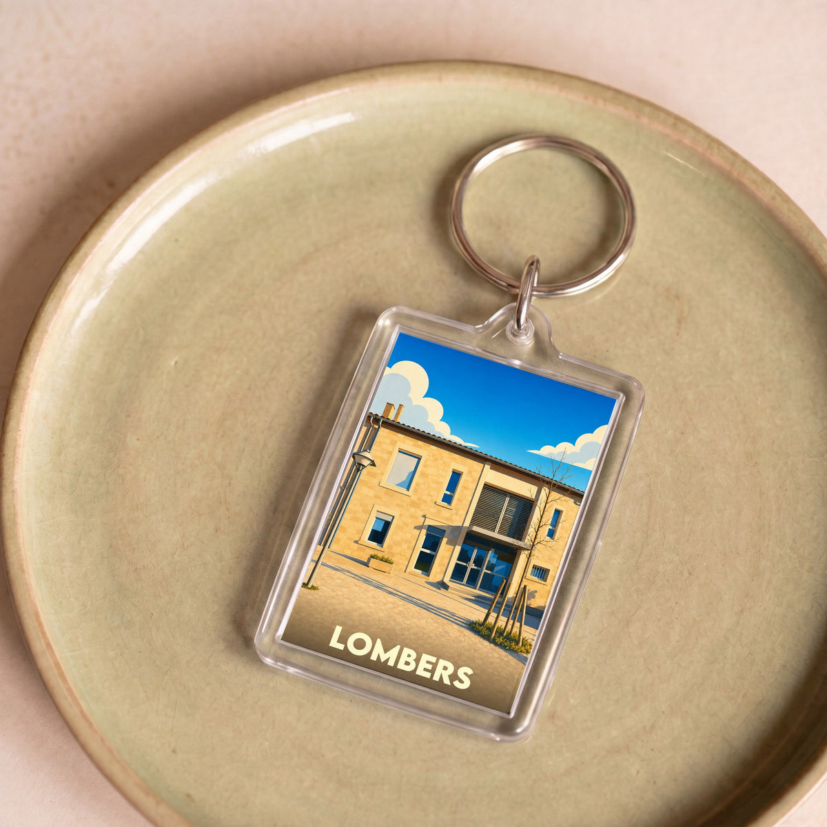 Porte-clés souvenir de la ville de Lombers avec une illustration stylisée d'un bâtiment local sous un ciel bleu.