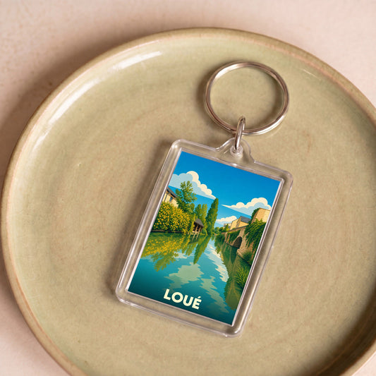Porte-clés souvenir de la ville de Loué avec une illustration stylisée des bords de la rivière.