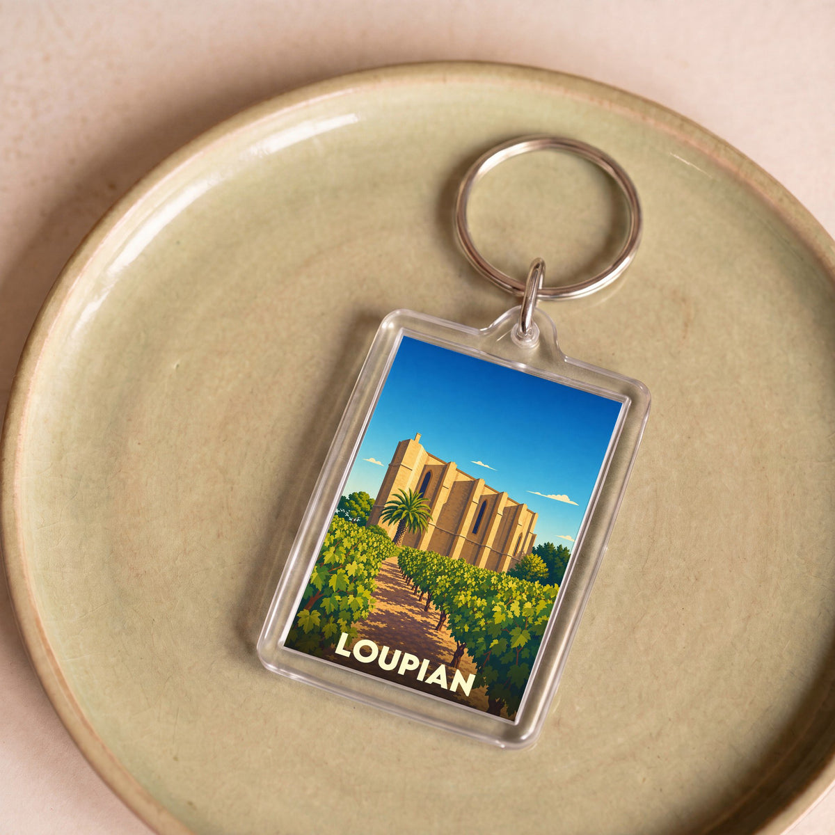 Porte-clés souvenir de la ville de Loupian avec une illustration stylisée d'une église et de vignes.