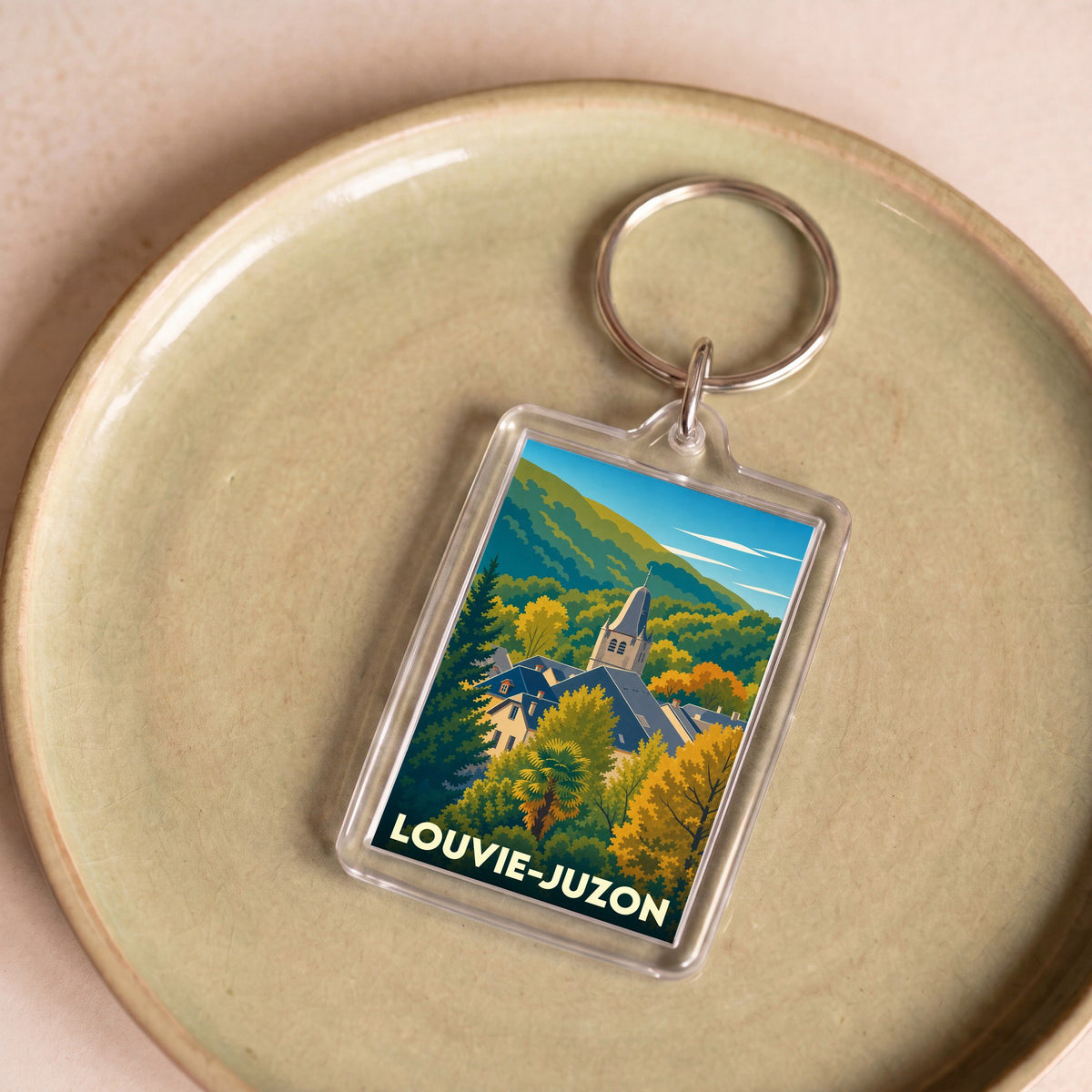 Porte-clés souvenir de la ville de Louvie-Juzon avec une illustration stylisée de son église et des montagnes environnantes.