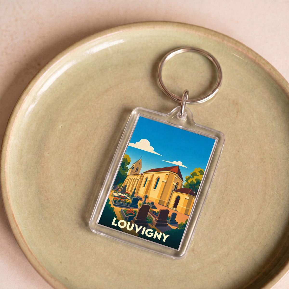 Porte-clés souvenir de la ville de Louvigny avec une illustration stylisée de son église et de son cimetière.