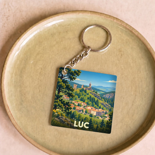 Porte-clés souvenir de la ville de Luc avec une illustration stylisée d'un village de montagne.