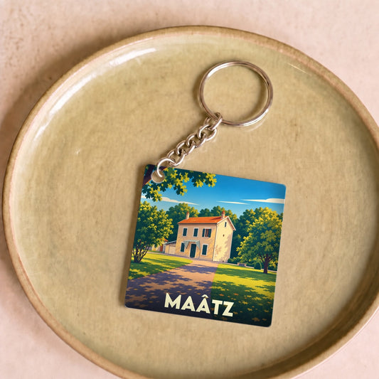 Porte-clés souvenir de la ville de Maâtz avec une illustration stylisée d'une maison ensoleillée.