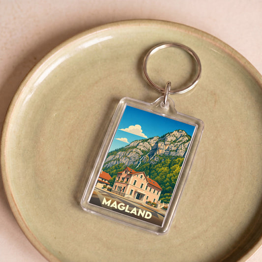 Porte-clés souvenir de la ville de Magland avec une illustration stylisée d'un paysage montagneux.