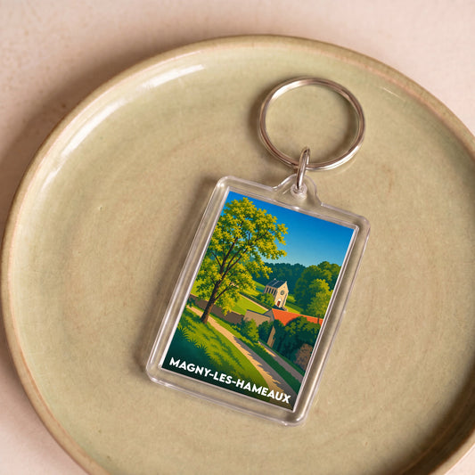 Porte-clés souvenir de la ville de Magny-les-Hameaux avec une illustration paysagère stylisée.