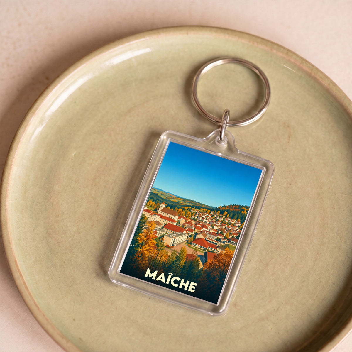 Porte-clés souvenir de la ville de Maîche avec une illustration stylisée de son paysage urbain en automne.