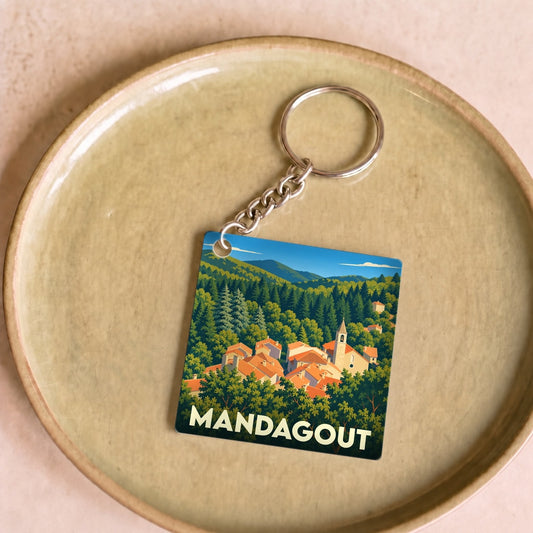 Porte-clés souvenir de la ville de Mandagout avec une illustration stylisée d'un village niché dans la forêt.