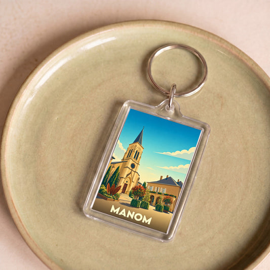 Porte-clés souvenir de la ville de Manom avec une illustration stylisée.