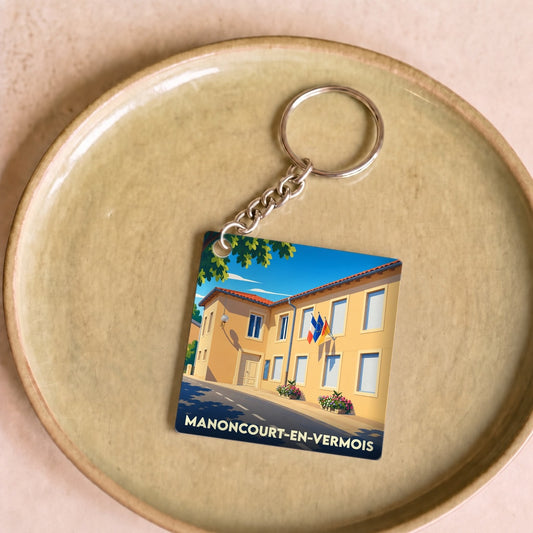 Porte-clés souvenir de Manoncourt-en-Vermois arborant une illustration stylisée de sa mairie.