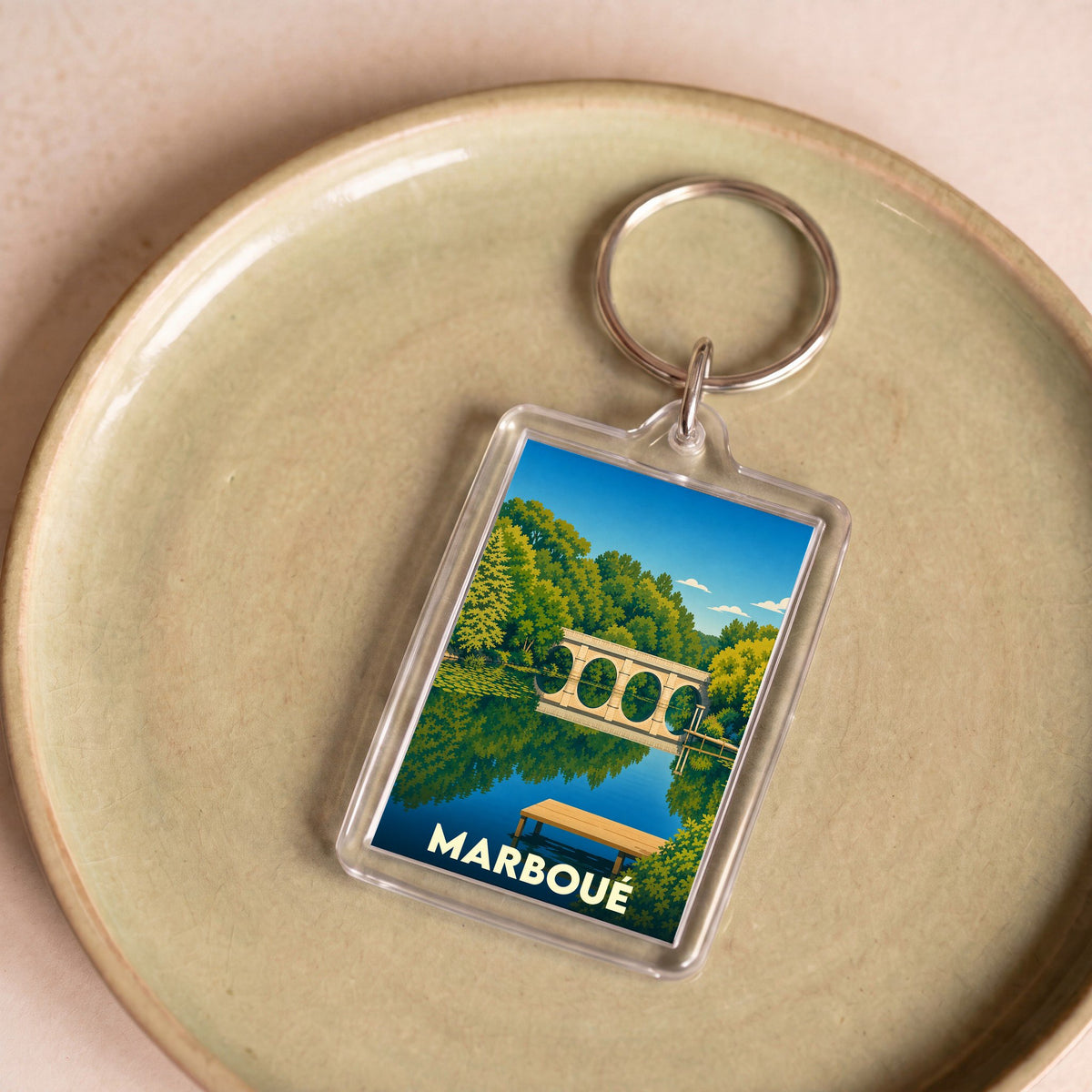 Porte-clés souvenir de la ville de Marboué avec une illustration stylisée d'un pont en pierre se reflétant dans l'eau.