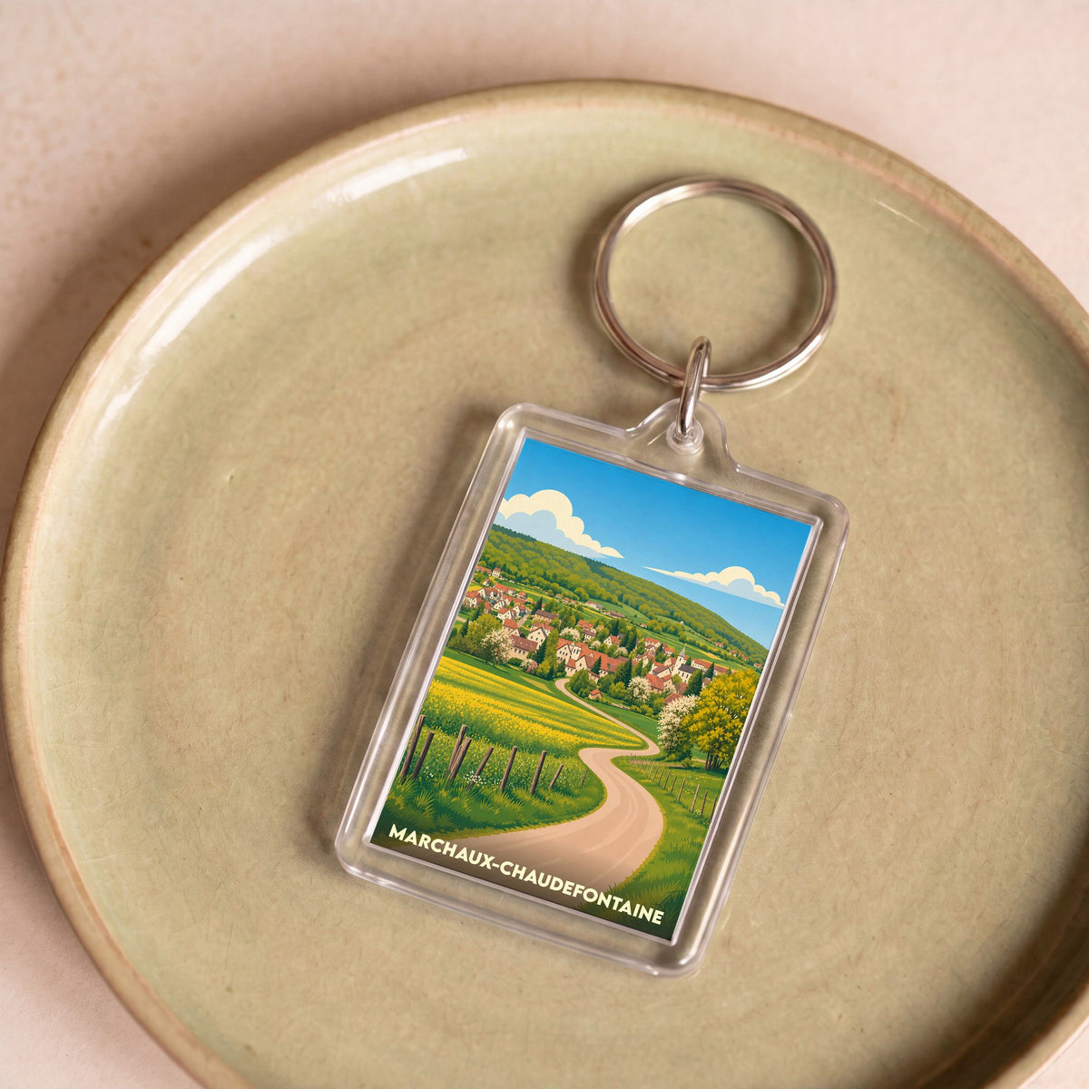 Porte-clés souvenir de la ville de Marchaux-Chaudefontaine avec une illustration stylisée de son paysage rural.