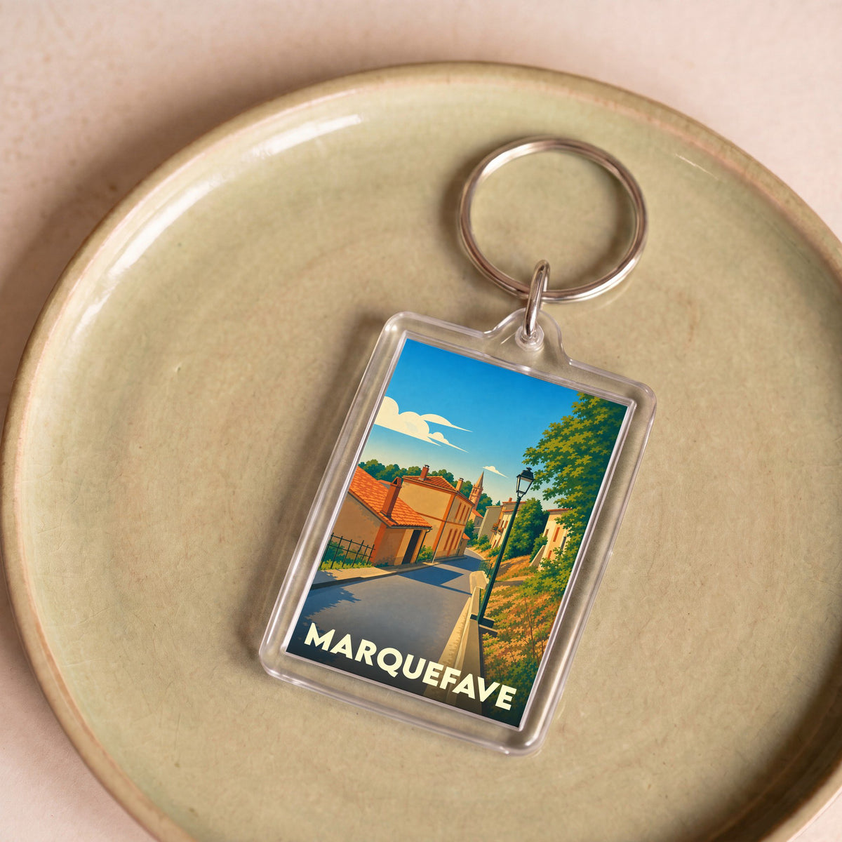 Porte-clés souvenir de la ville de Marquefave avec une illustration stylisée d'une rue ensoleillée.