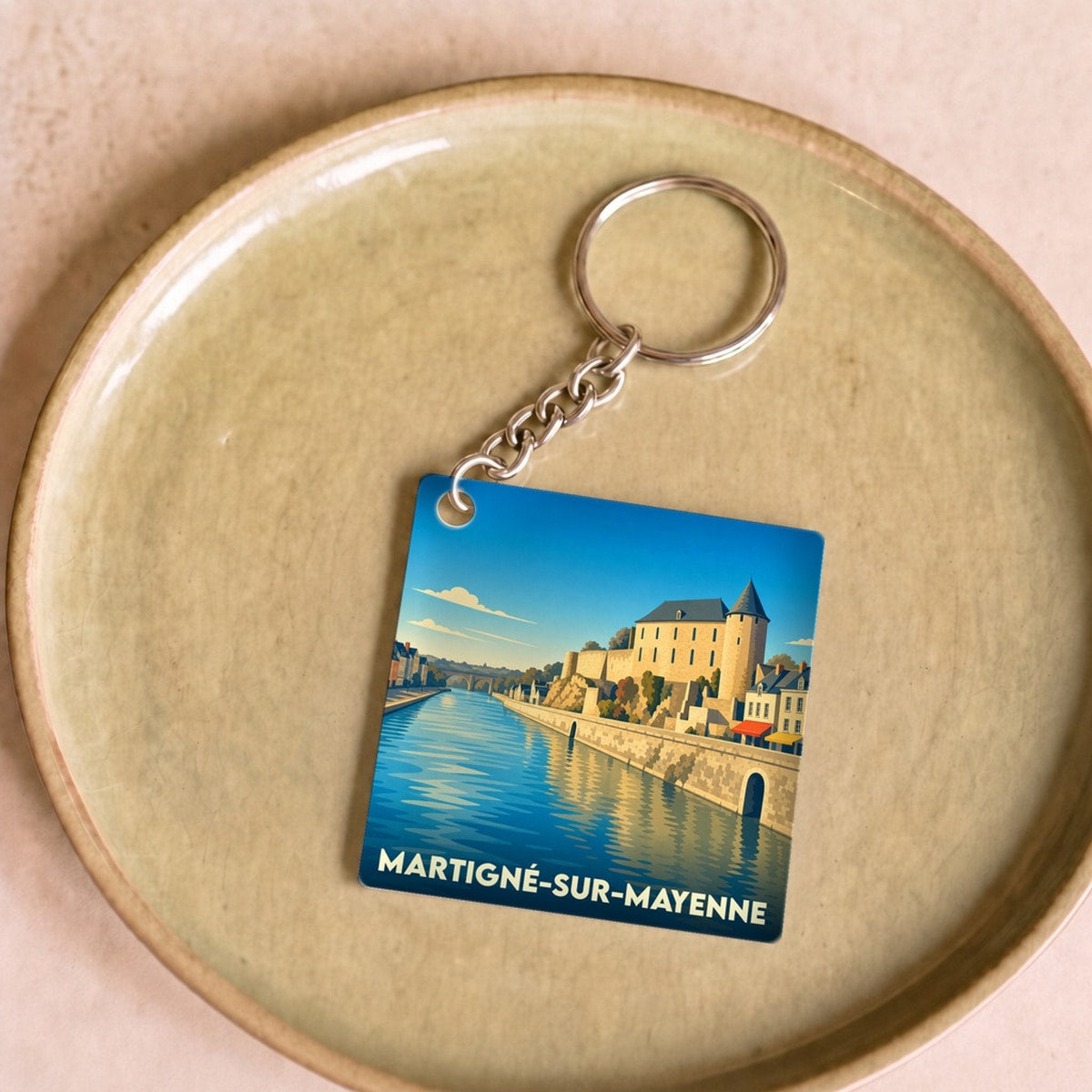 Porte-clés souvenir de Martigné-sur-Mayenne avec une illustration stylisée de la ville au bord de l'eau.