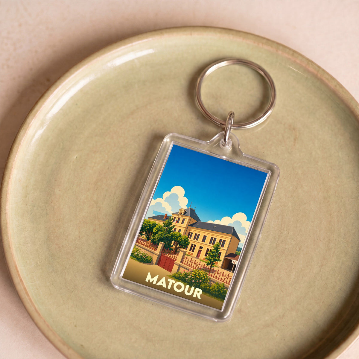 Porte-clés souvenir de la ville de Matour avec une illustration stylisée d'un bâtiment historique sous un ciel bleu.