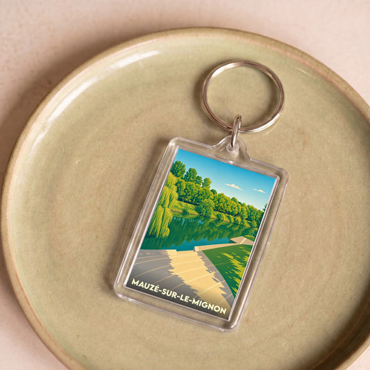 Porte-clés souvenir de la ville de Mauzé-sur-le-Mignon avec une illustration stylisée d'un bord de rivière.