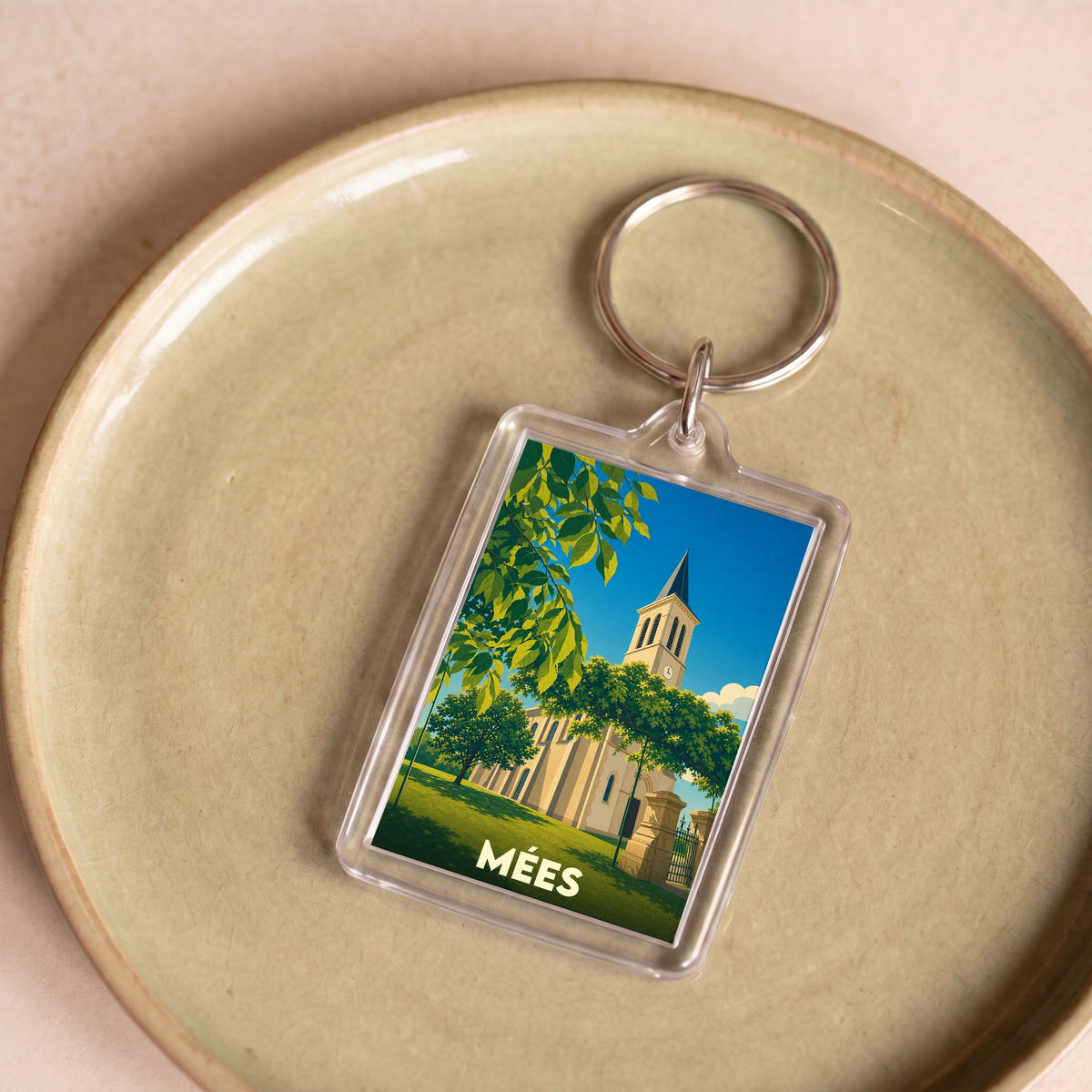 Porte-clés souvenir de la ville de Mées avec une illustration stylisée d'une église sous un ciel bleu.