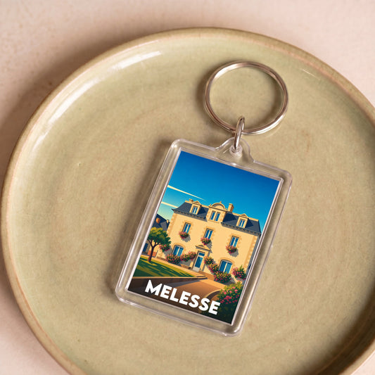 Porte-clés souvenir de la ville de Melesse avec une illustration stylisée d'un bâtiment fleuri.