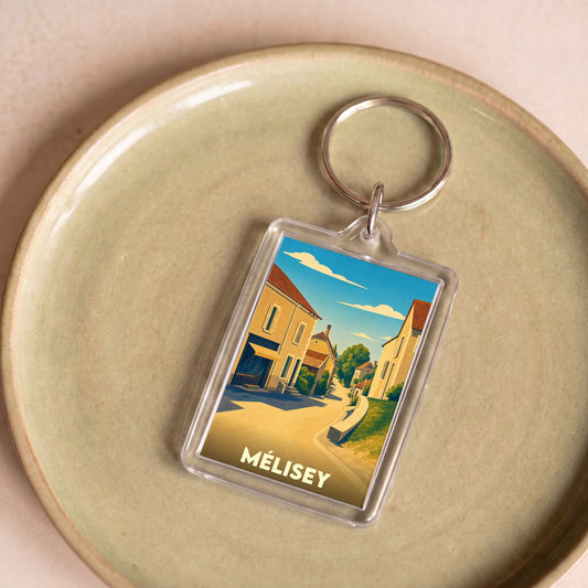 Porte-clés souvenir de la ville de Mélisey avec une illustration stylisée d'une rue ensoleillée.