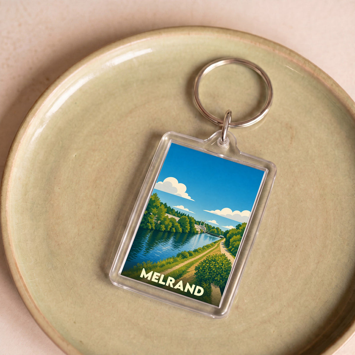 Porte-clés souvenir de la ville de Melrand avec une illustration stylisée d'un paysage de rivière.