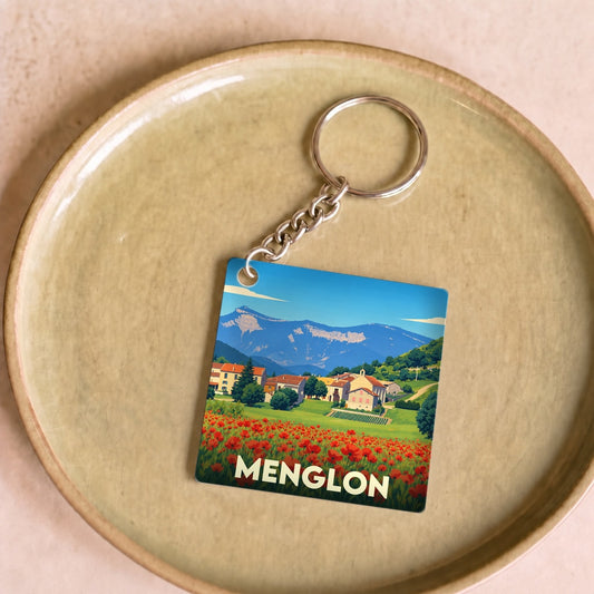 Porte-clés souvenir de la ville de Menglon avec une illustration stylisée d'un champ de coquelicots devant un village de montagne.