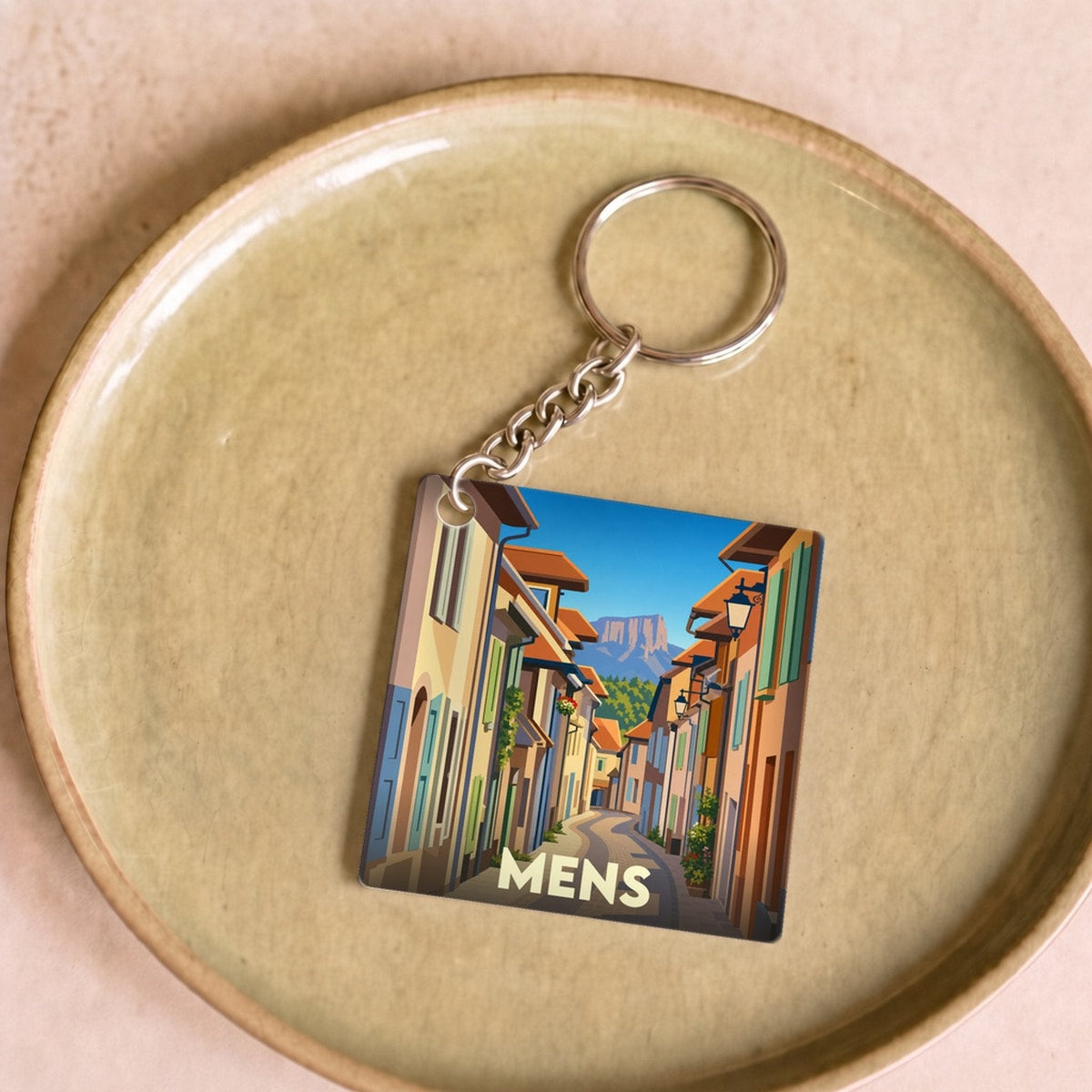 Porte-clés souvenir de la ville de Mens avec une illustration stylisée d'une rue pittoresque.