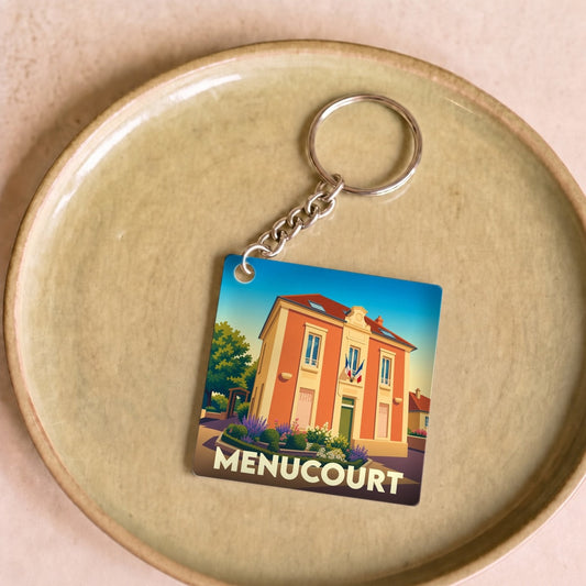 Porte-clés souvenir de la ville de Menucourt avec une illustration stylisée de la mairie.