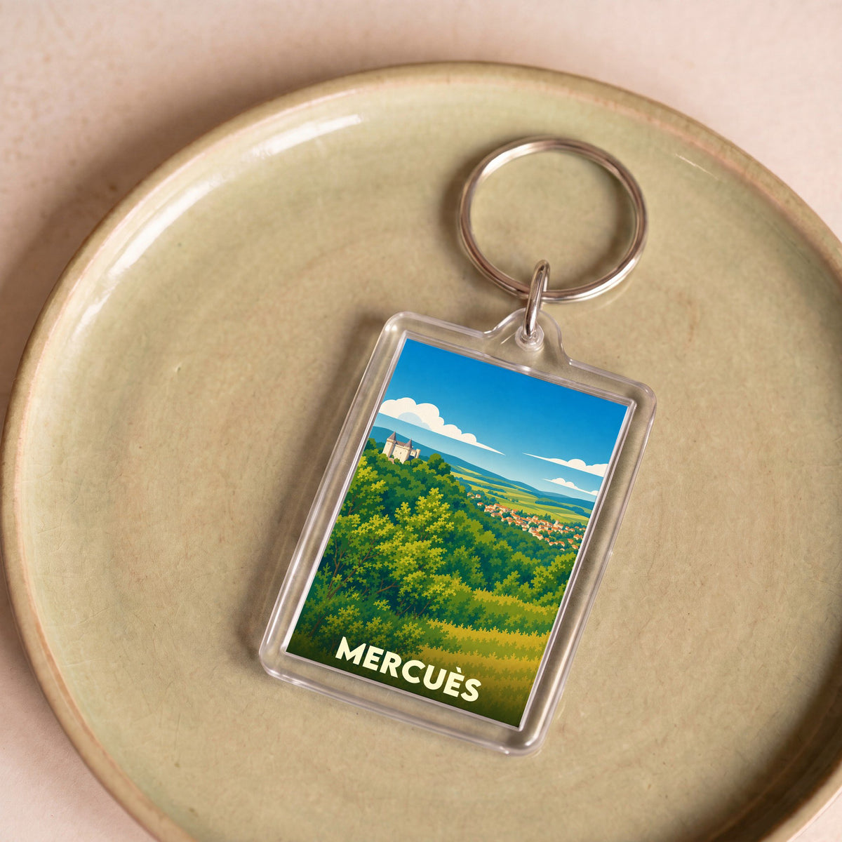 Porte-clés souvenir de la ville de Mercuès avec une illustration stylisée de son château et de son paysage.