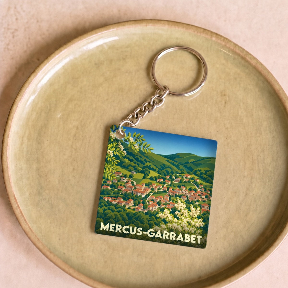Porte-clés souvenir de la ville de Mercus-Garrabet avec une illustration stylisée de son paysage vallonné.