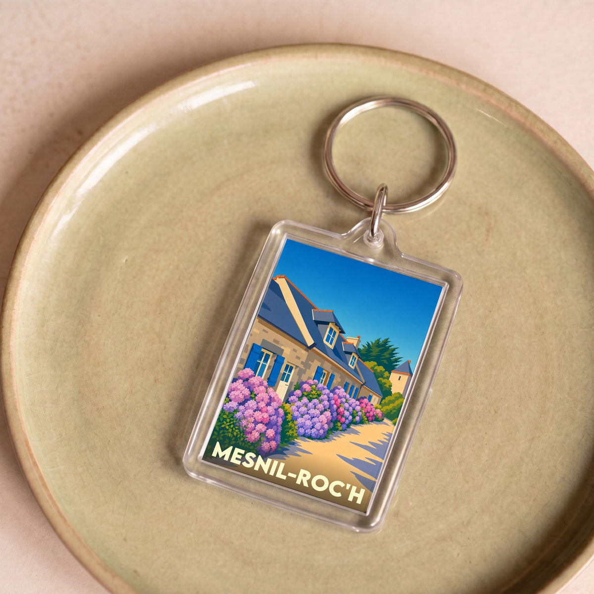 Porte-clés souvenir de la ville de Mesnil-Roc'h avec une illustration stylisée d'une maison fleurie.