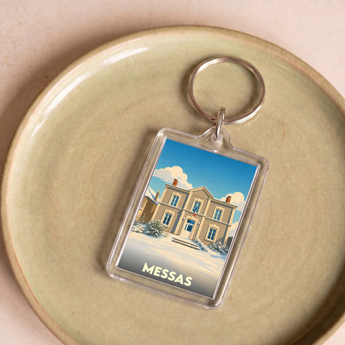 Porte-clés souvenir de la ville de Messas avec une illustration stylisée d'un bâtiment sous la neige.